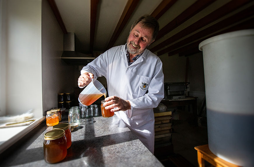 Inside workshop pouring honey from jug into a jar by Polly Baldwin