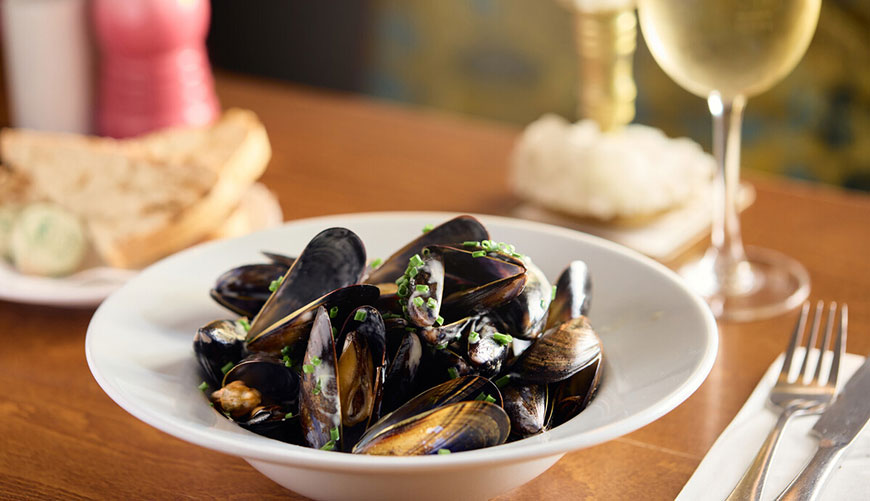 Bowl of mussels with glass of wine in background
