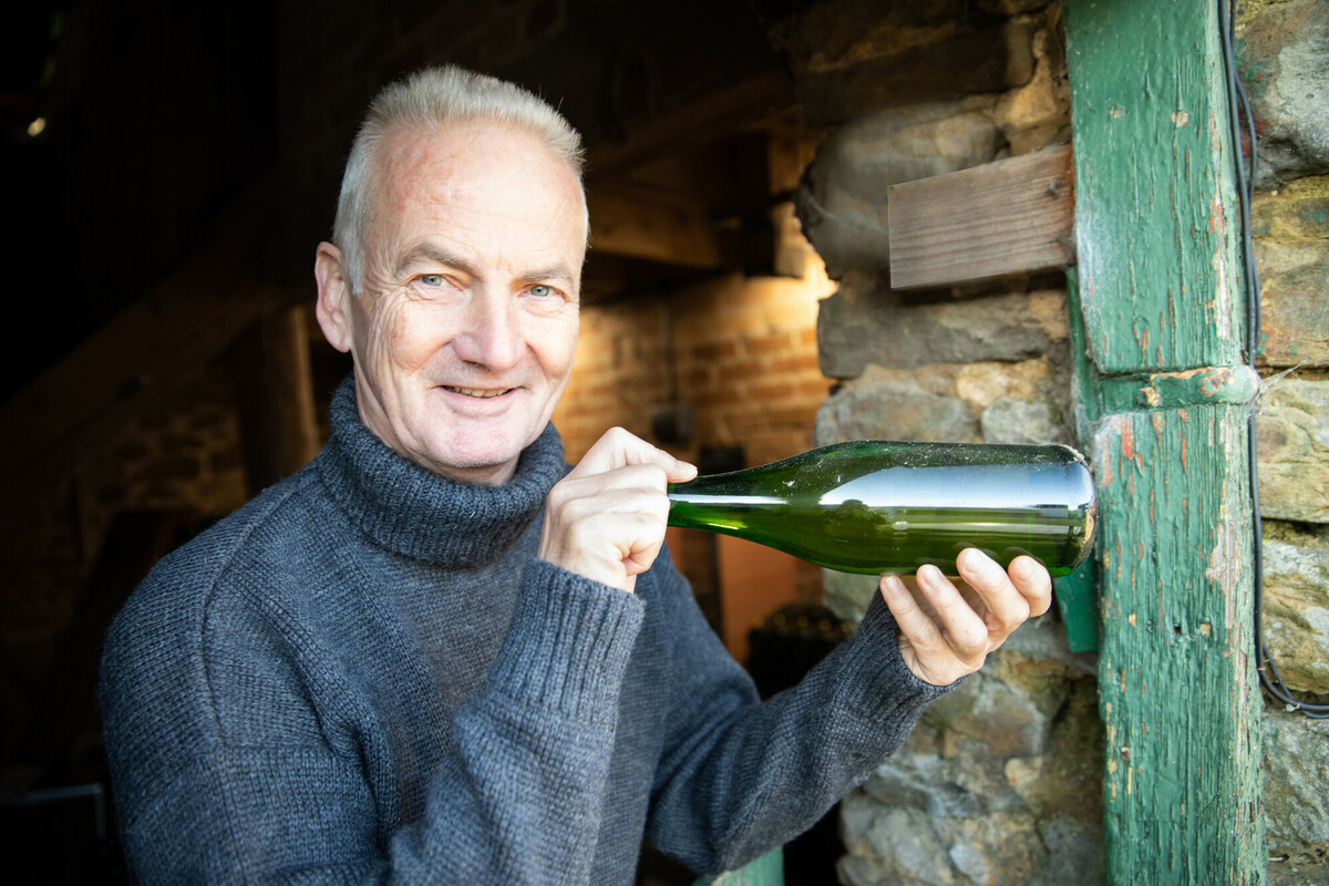 Male holding up a cider bottle at the entrance of a barn. Credit Charlie Fox.