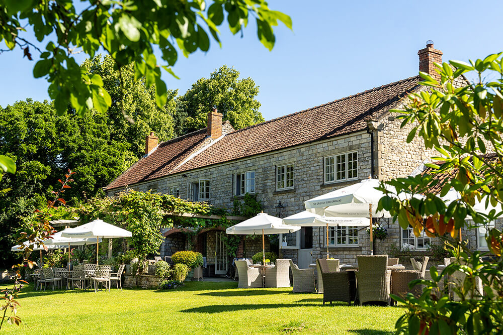 The exterior of The Pheasant with a lawn and chairs under umbrellas.