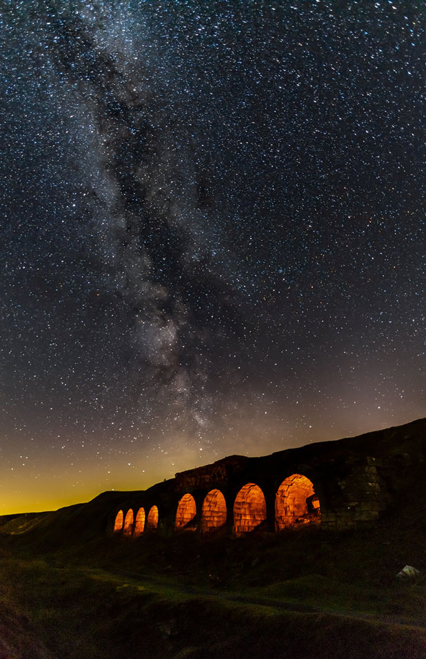 Nighttime photo of an old industrial building that has a series of stone arches Nighttime photo of an old industrial building that has a series of stone arches