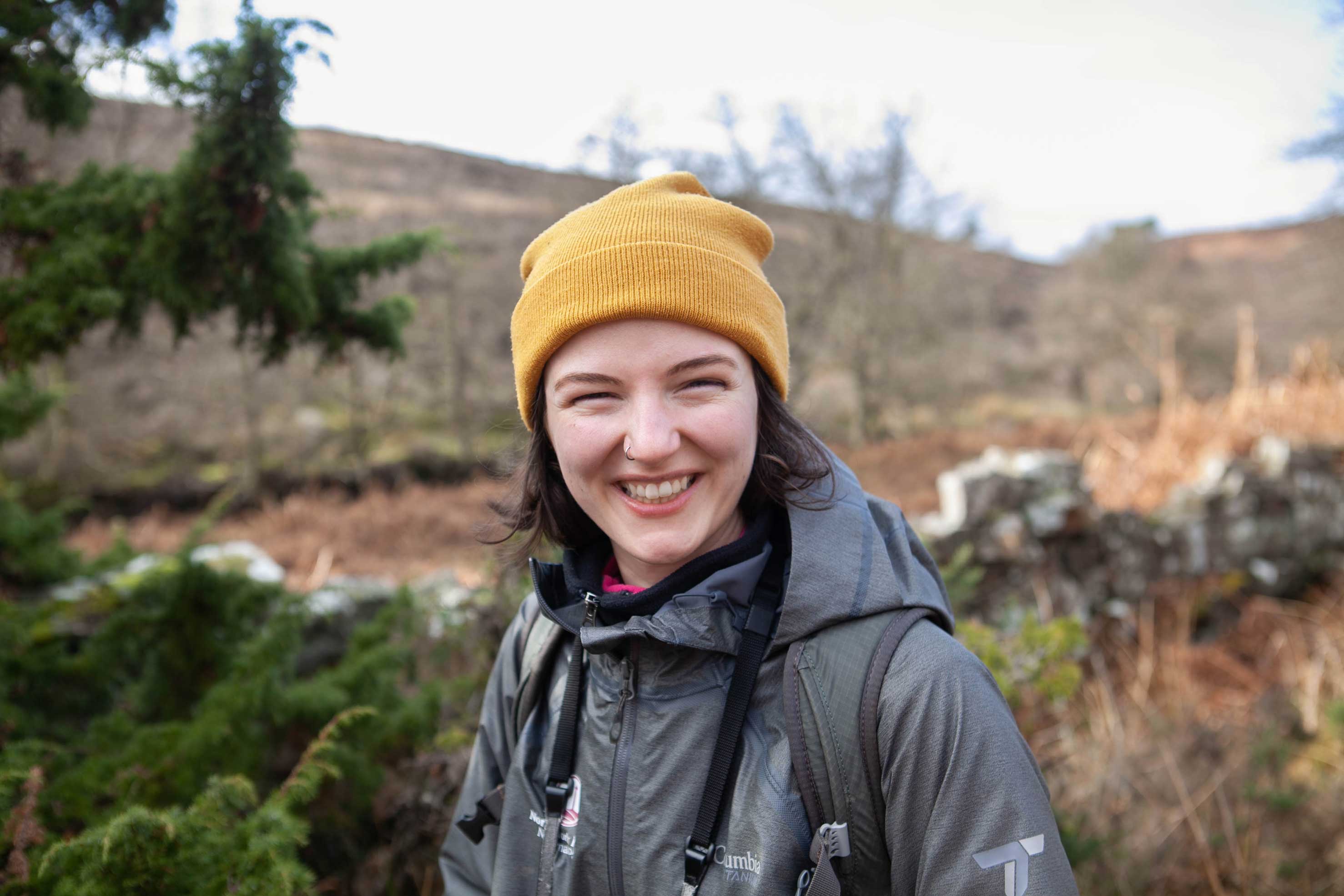 Woman wearing a yellow beanie standing among a moorland landscape. Credit Charlie Fox.