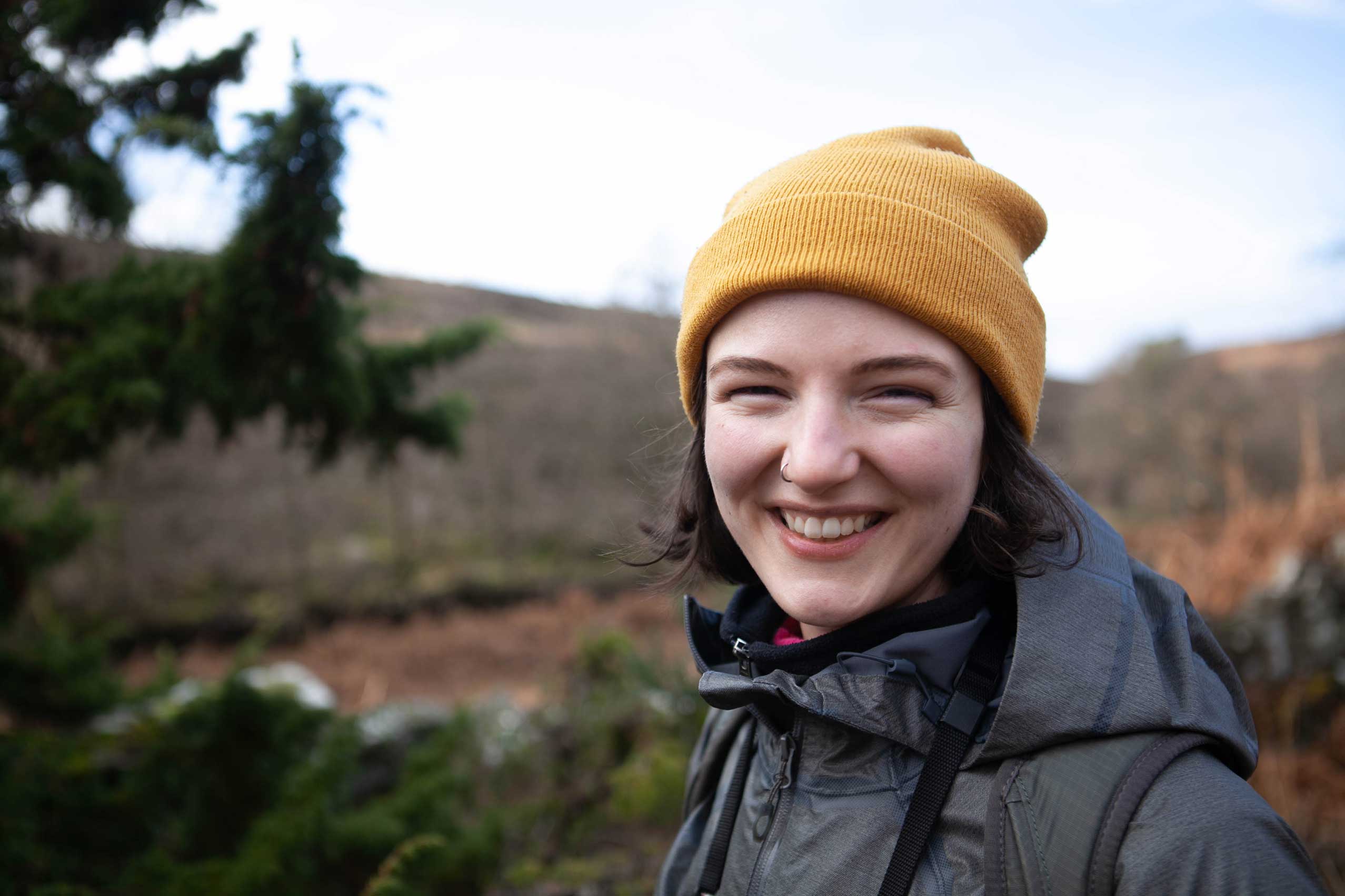 Woman wearing a yellow beanie standing among a moorland landscape. Credit Charlie Fox.