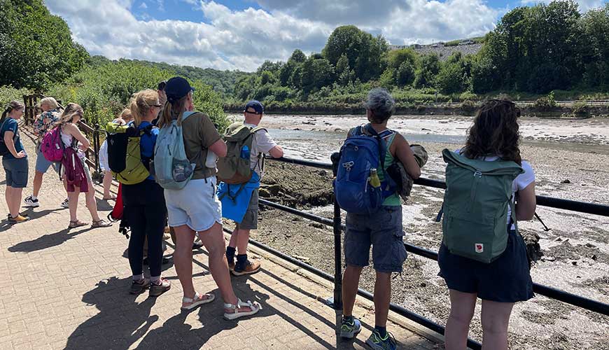 People stand at a barrier, looking over across the river.