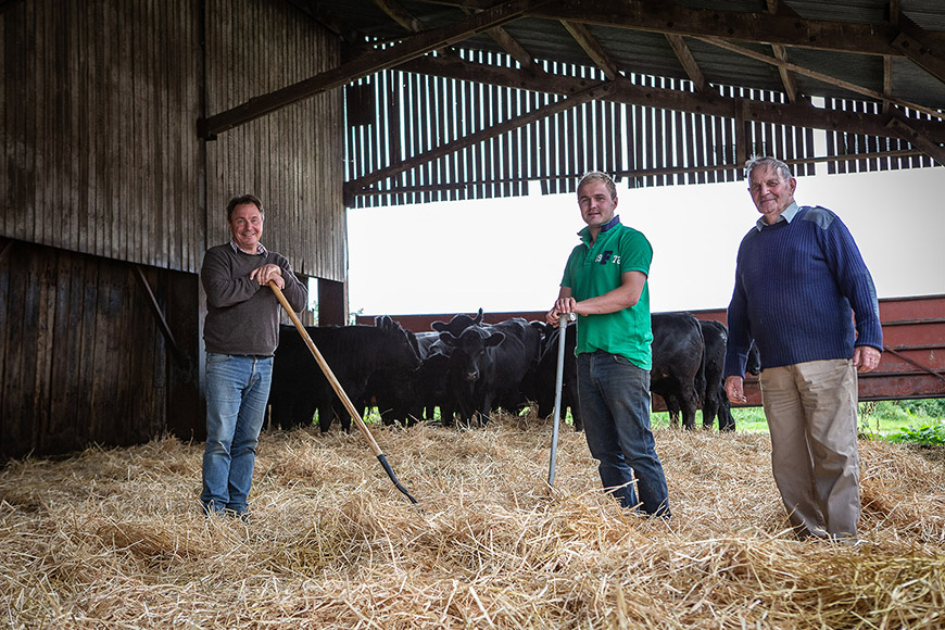 Three farmers stood in shed raking straw by Polly Baldwin