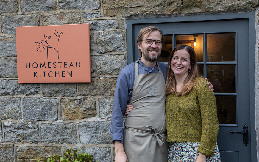 Peter and Cecily stood outside front door beside Homestead Kitchen sign by Polly Baldwin Peter and Cecily stood outside front door beside Homestead Kitchen sign by Polly Baldwin