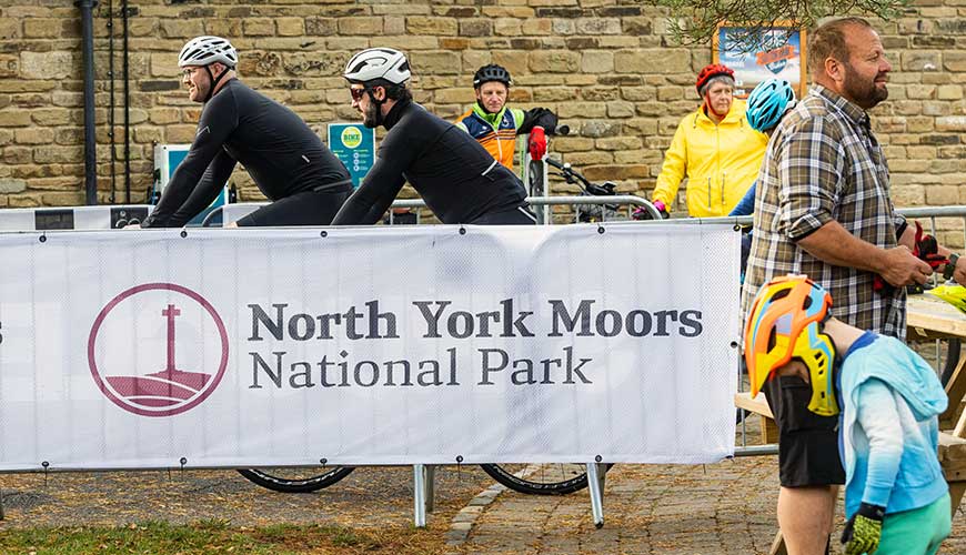 Two cyclists behind North York Moors National Park banner