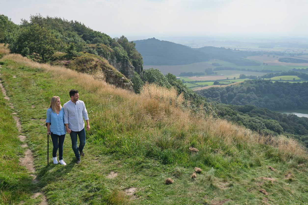 Two people walking alongside a cliff face. Credit VisitBritain/Daniel Wildey.
