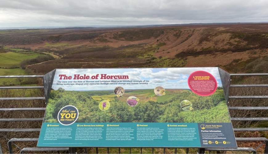 An information board about the Hole of Horcum, attached to a metal frame and overlooking a vast open, moorland