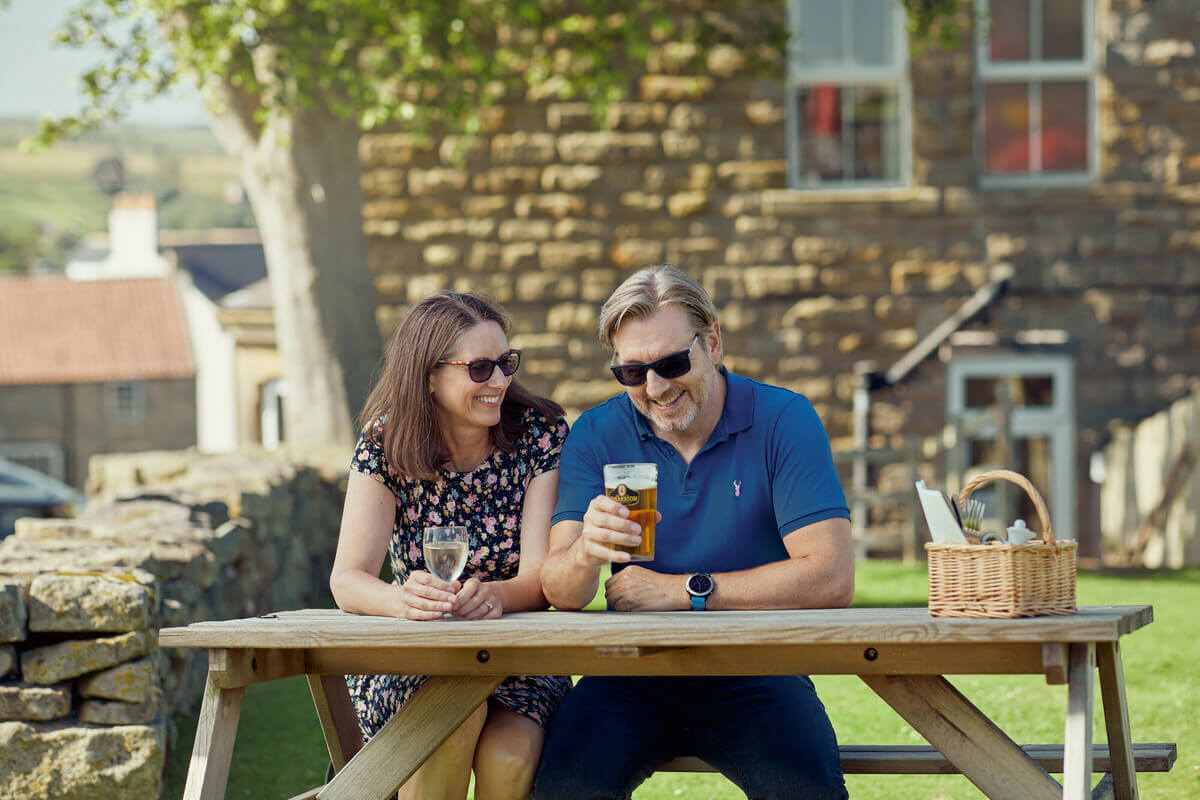A couple sat in a pub garden enjoying a glass of beer.