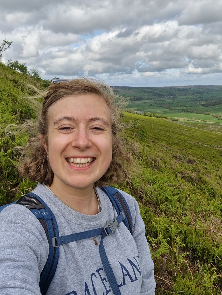 A selfie of Gabriella with a green hilly backdrop. 