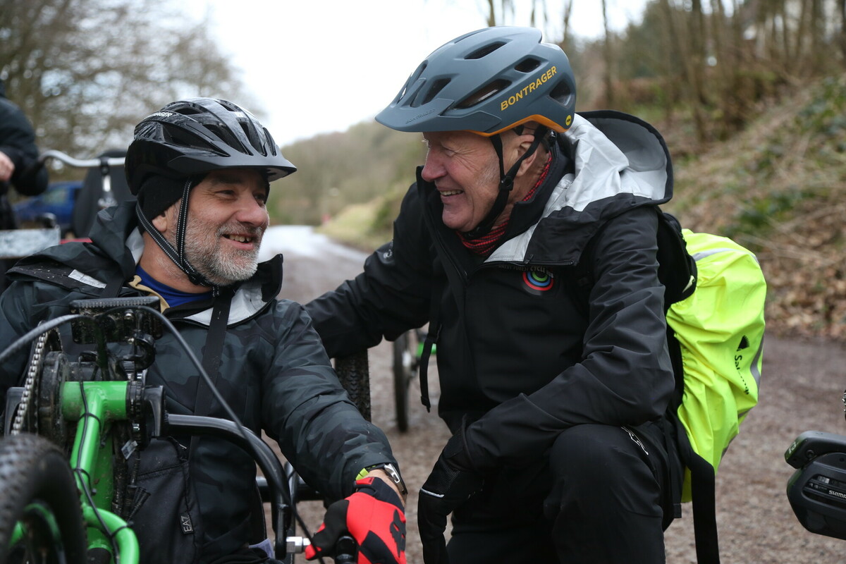 Rob Brown and Simon smiling at each other on a bike