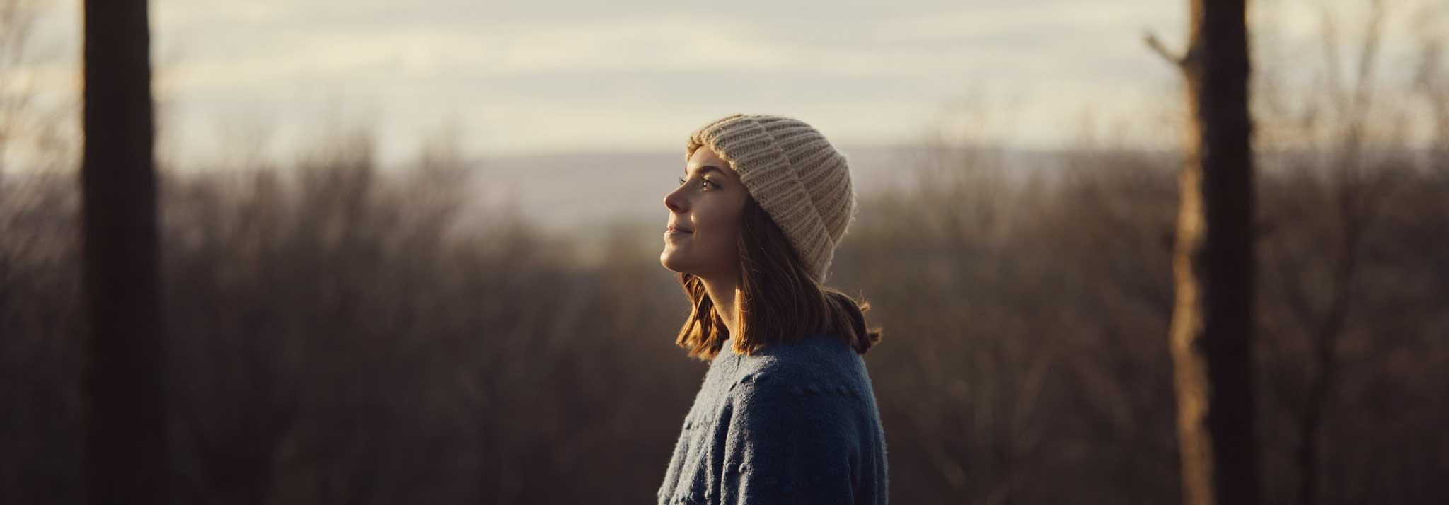 A women reflecting and looking into the distance among a woodland in autumn. Credit Olivia Brabbs Photography. 