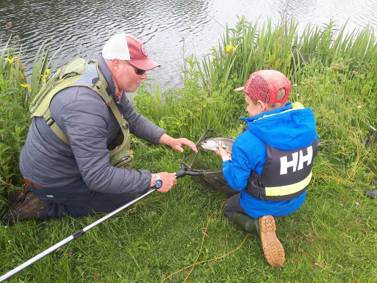 Man and young child inspect a fish of catching it with a net. Man and young child inspect a fish of catching it with a net.