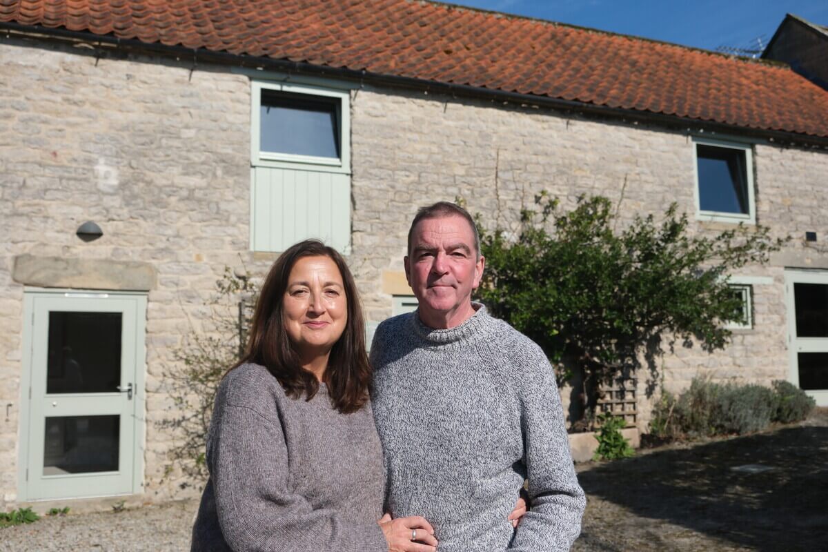 A woman and a man stand arm in arm outside their BnB.