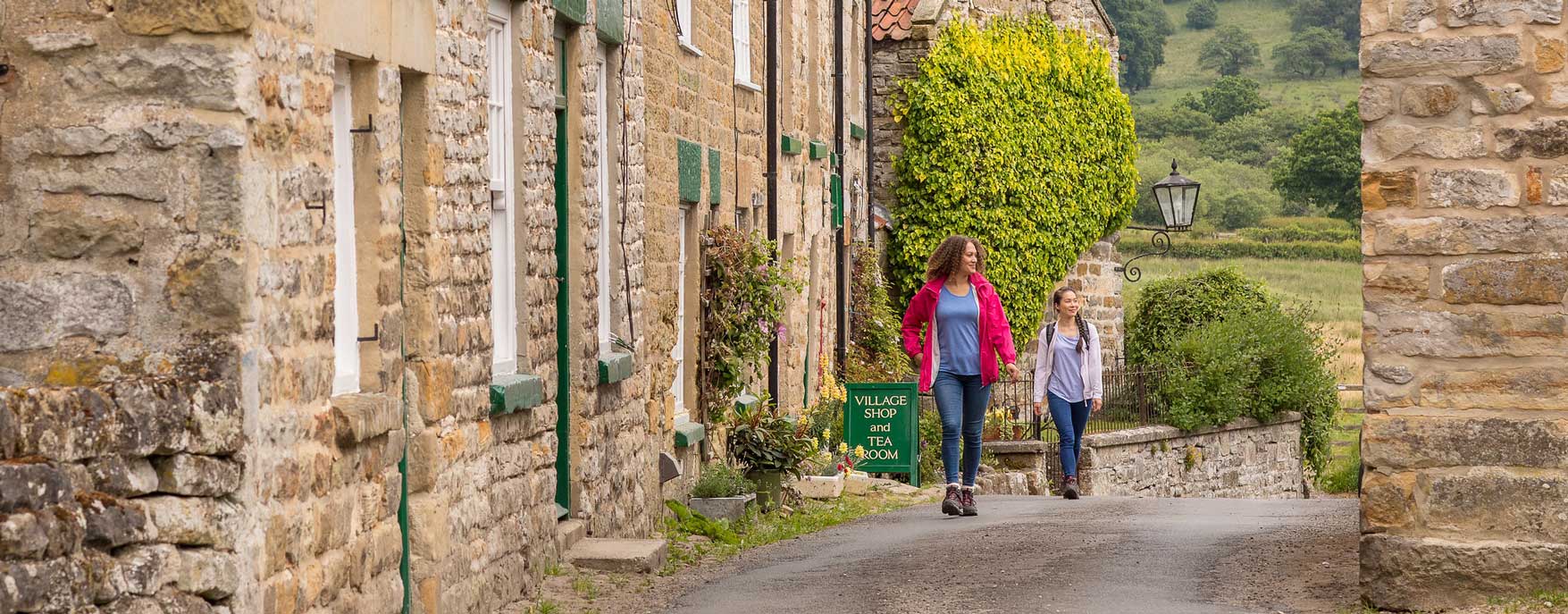 Two women walking between traditional stone building. Credit Dependable Productions.