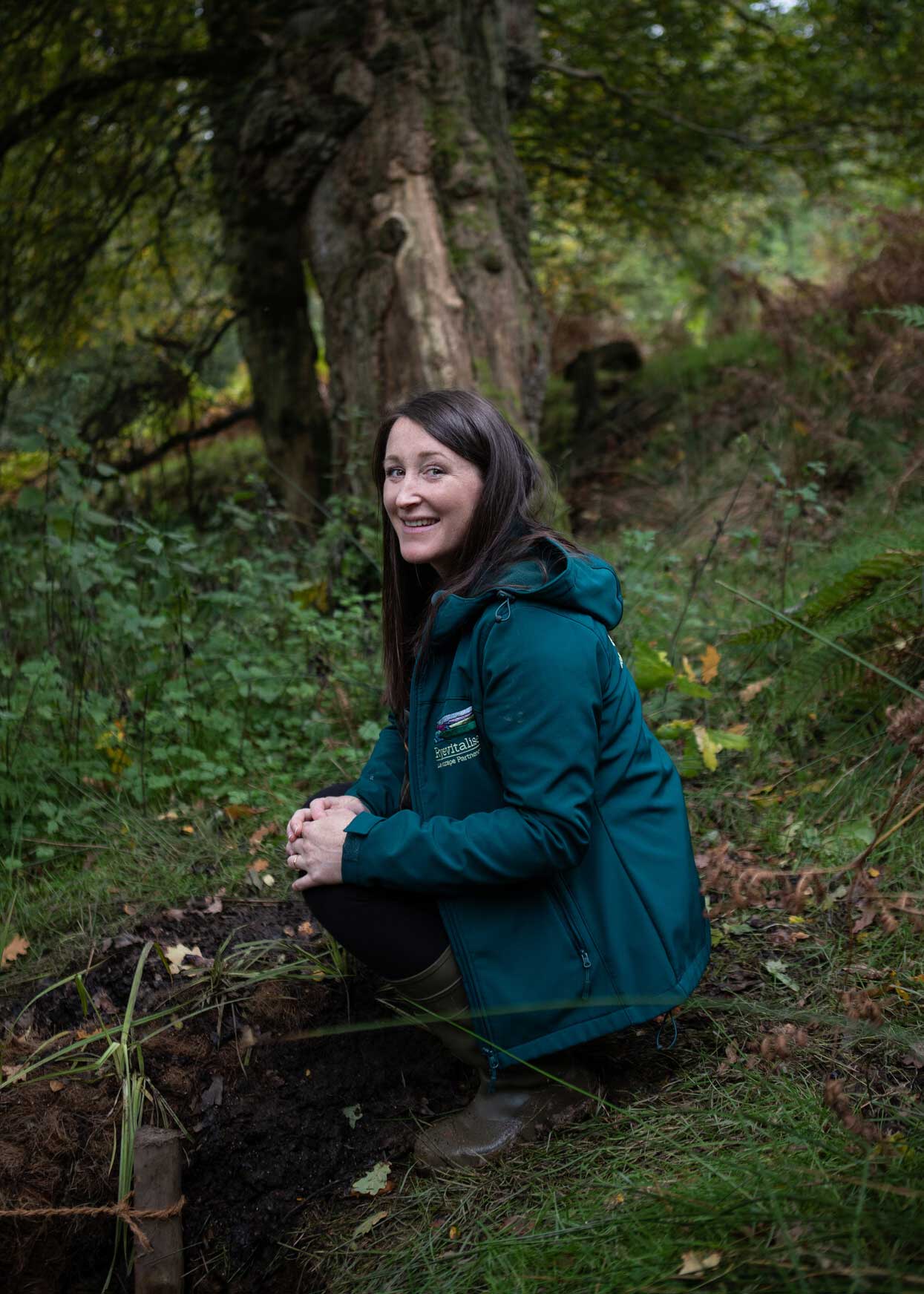 Female in a dense woodland. She is crouched near a small flow of water heading downhill. Credit Charlie Fox.
