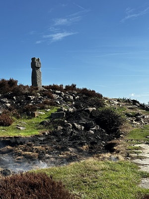 Lilla cross stands on grassy hill, charred smoking ground can be seen in the foreground 