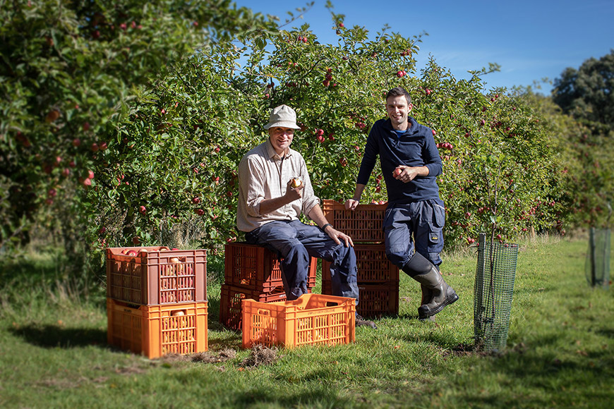 Orchard workers sat and leant against crates filled with apples in the orchard by Polly Baldwin