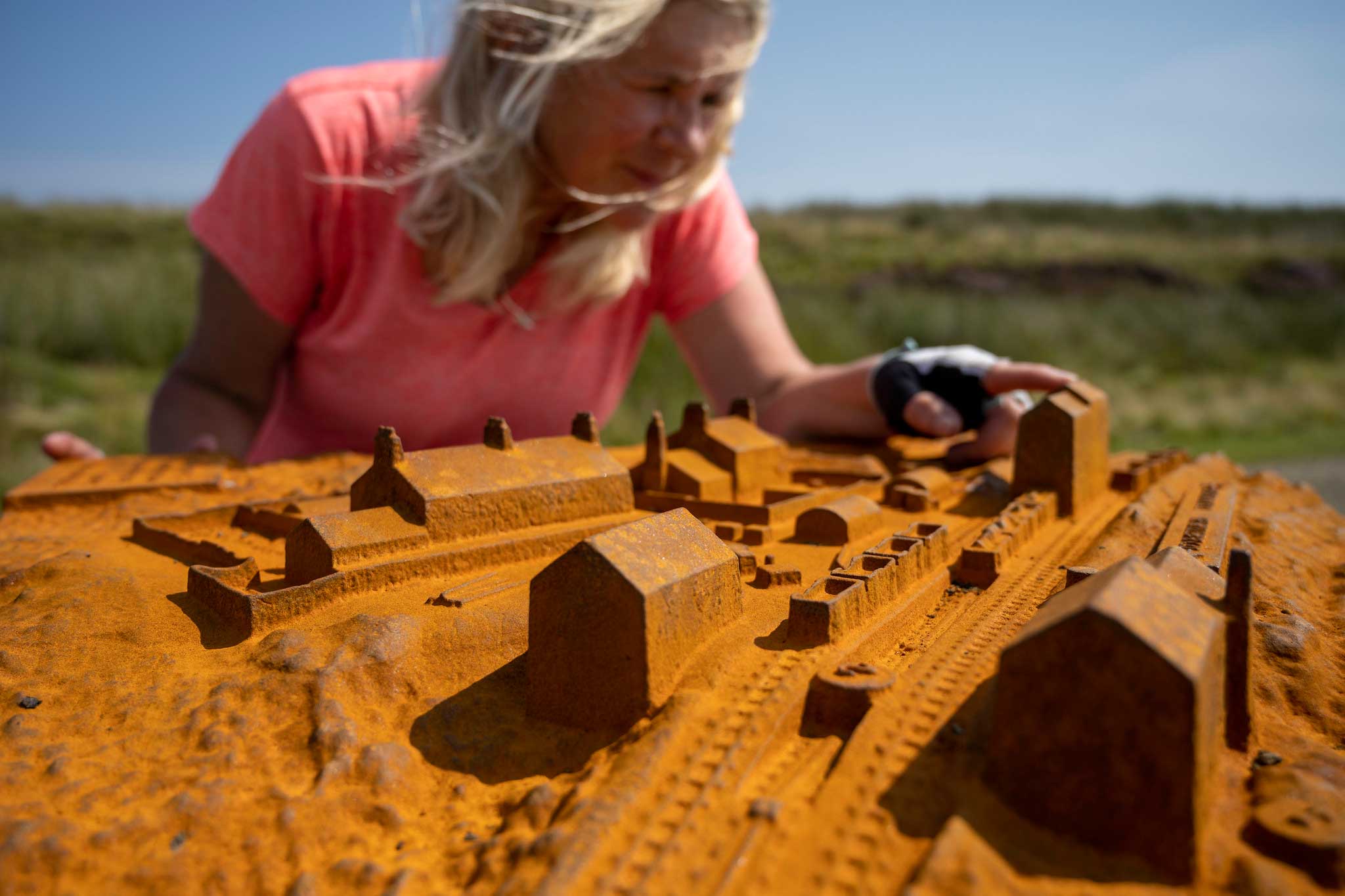 Photo of a cyclist looking closely at a cast iron model in a rural landscape