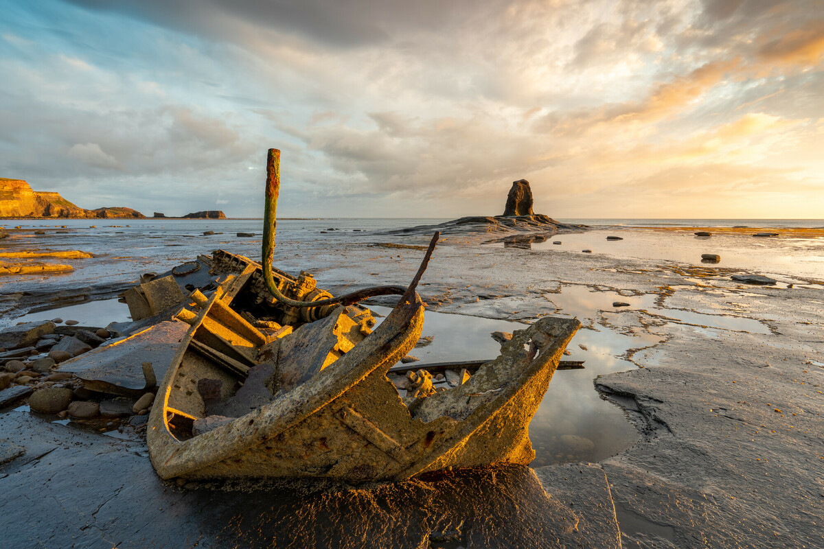 Ruins of a metal ship along a coastline. Credit Oliver Sherratt.