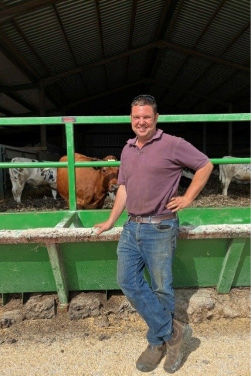 Richard of Wethercote Farm Person in a purple polo shirt standing beside a green cattle pen with several cows behind him.