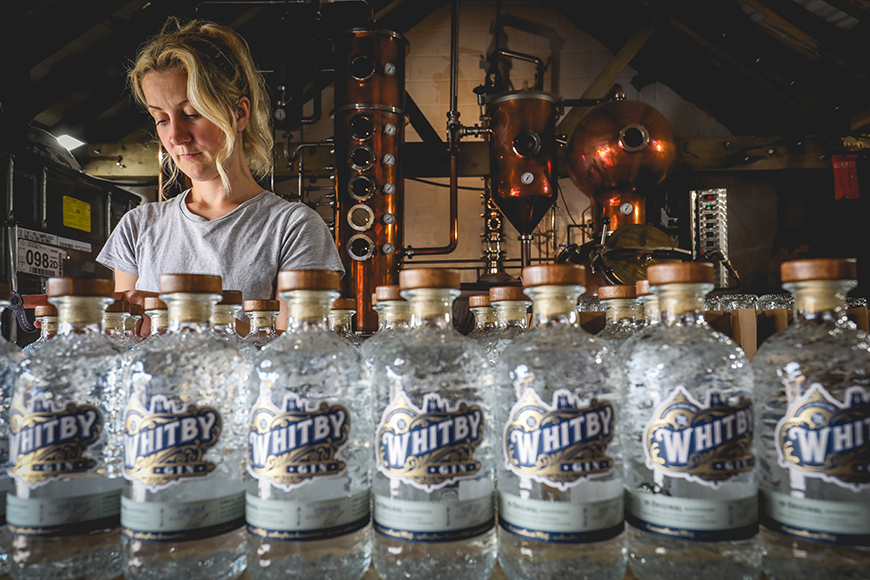 Gin bottles lined up with distillers in the background by Ceri Oakes