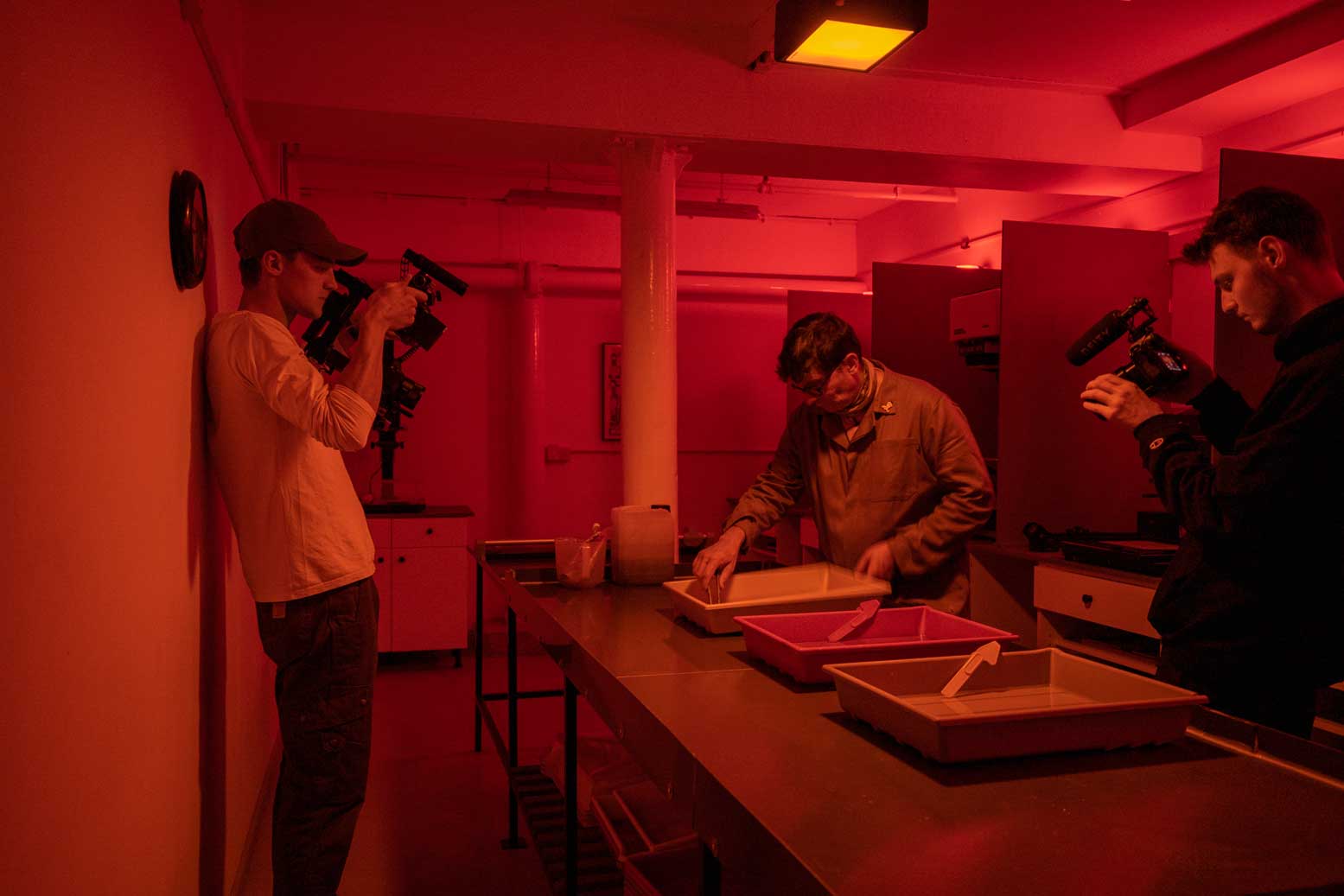 Artist working in a darkroom. Two men are filming what he does. Credit 2B13 Productions.