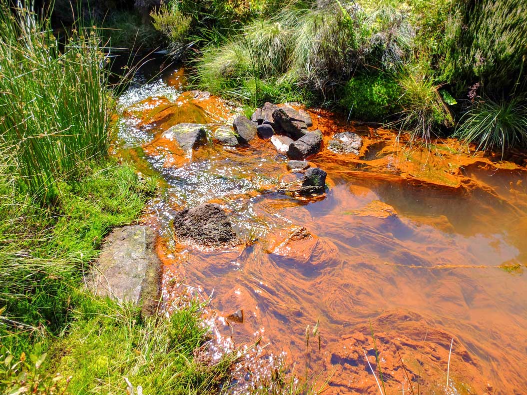 Photo showing mine discharge among a river. It has left an orange / rust coloured appearance within the water.
