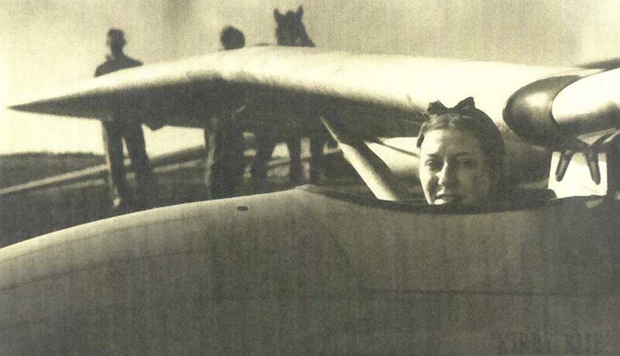 A sepia image of a person in the cockpit of a plane. The image is from the 1930s and the person featured is Amy Johnson.