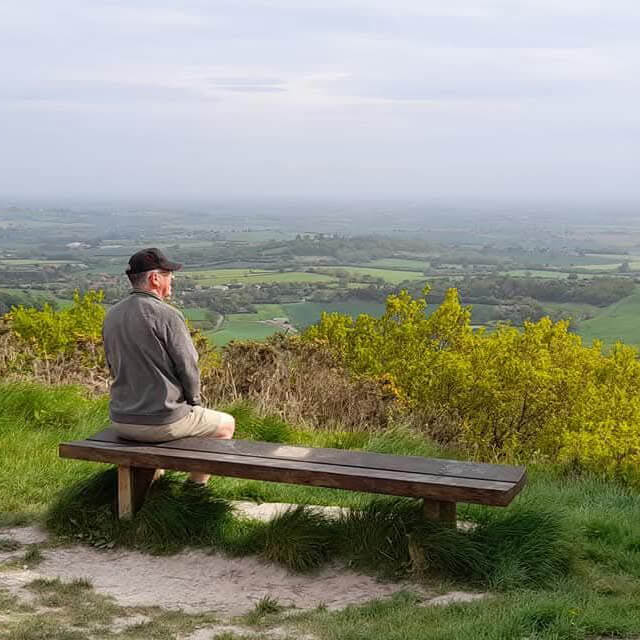 A man sat on a bench looking out toward Vale of Mowbray.