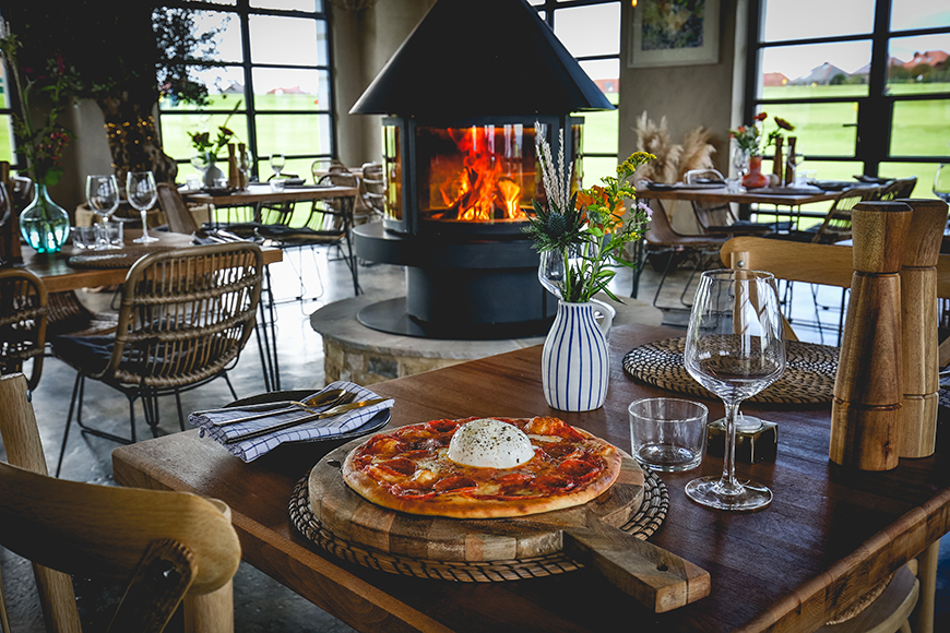 Pizza on a plate in the restaurant with lit fire in the background by Ceri Oakes