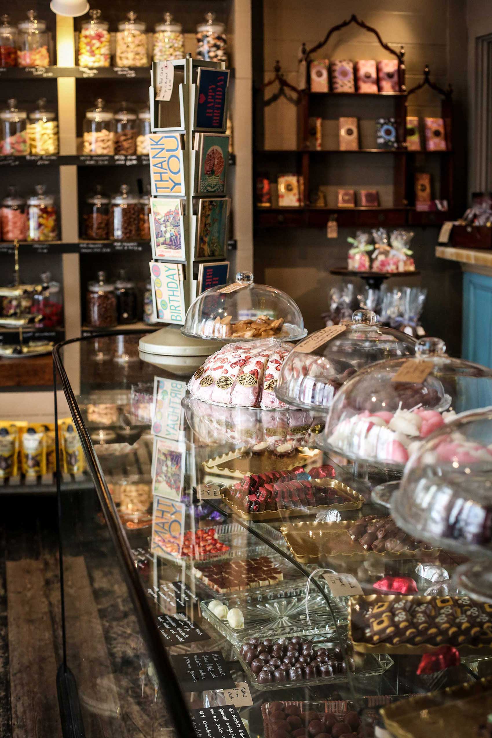 Glass counter filled with chocolates and shelves in the background filled with sweets by Polly Baldwin