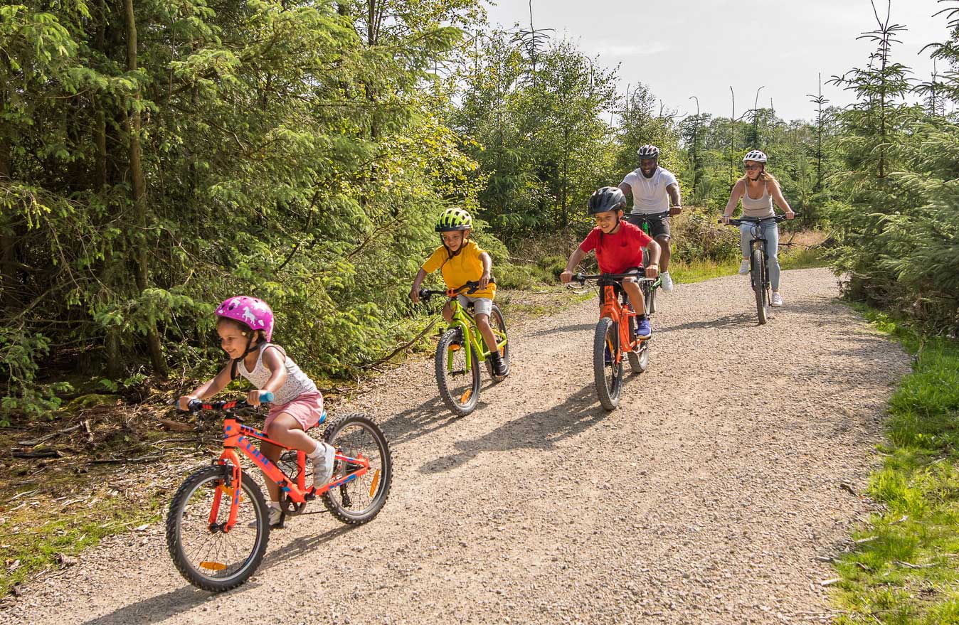 Family biking down a gravel track among woodland. Credit Dependable Productions.