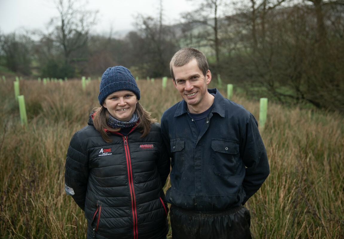 Amanda and Mark Smith standing in the foreground with a woodland creation scheme in the background. Credit Charlie Fox.