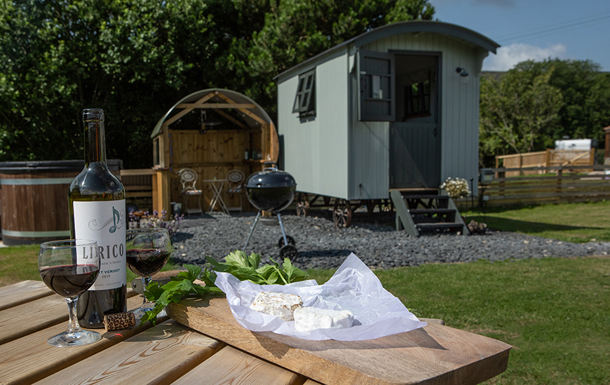 Goats cheese on a wooden board next to red wine. Shepherd's hut in the background by Polly Baldwin