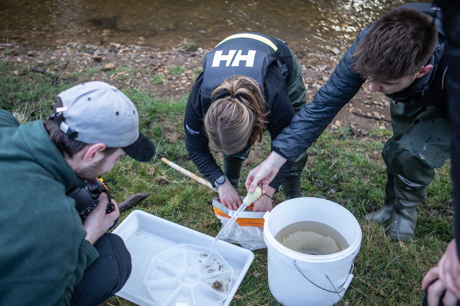 Group of people inspecting the contents of a white tray as part of a riverfly survey. Credit Charlie Fox.