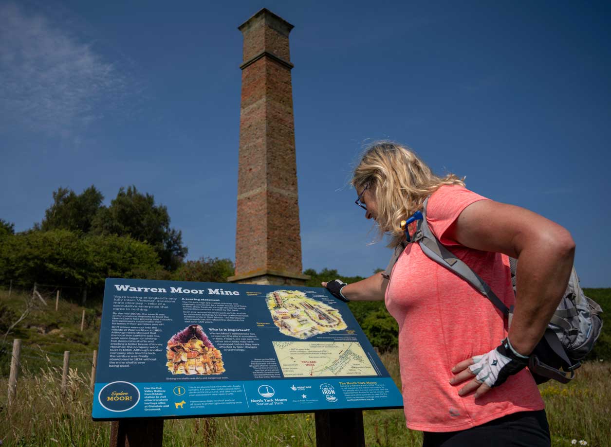 Cyclist looking at an interpretation panel explaining the history of a tall industrial tower in front of it.