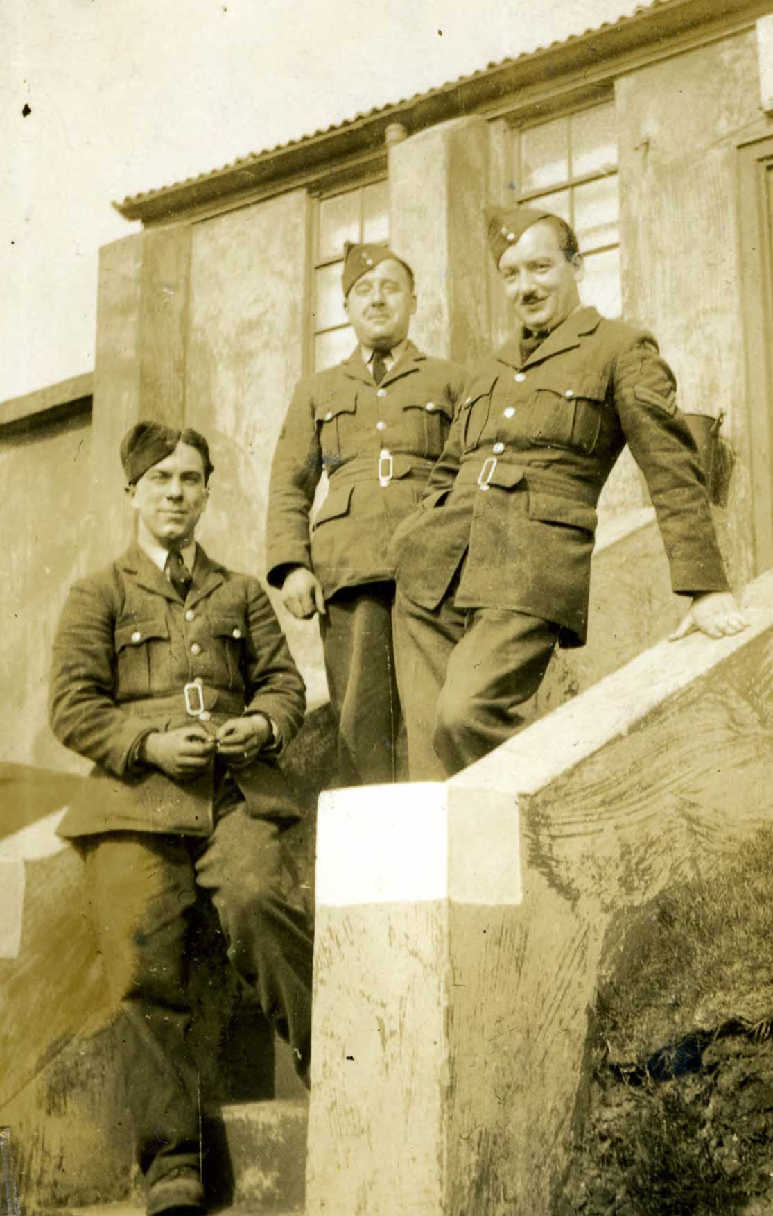 Black and white photograph of three men stood on some steps.