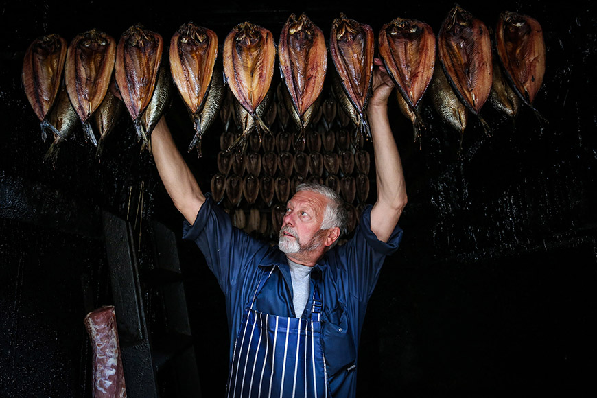 Man placing a rack full of kippers on the ceiling by Ceri Oakes