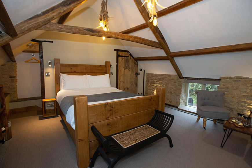 Bedroom with wooden beams and wooden double bed by Polly Baldwin