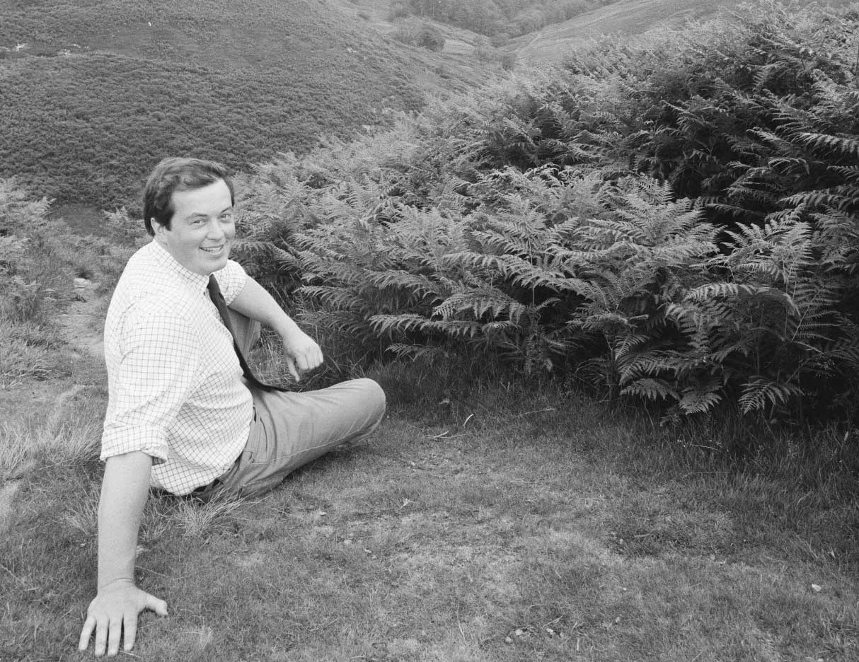 Man sitting on the edge of a moorland near bracken.