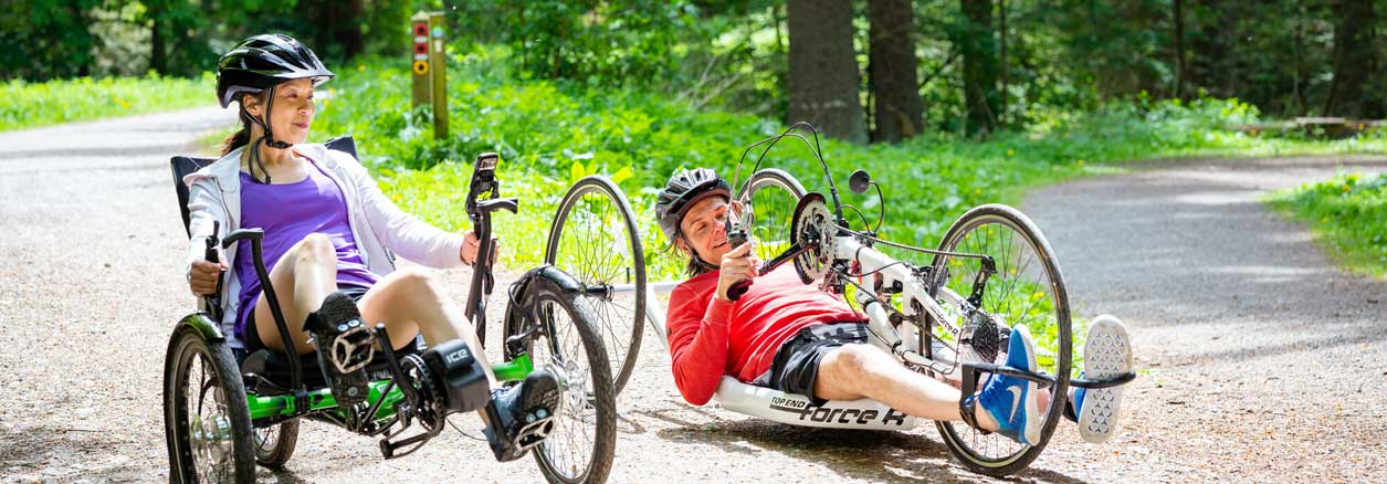 Two people ridding recumbent ebikes in a woodland setting. Credit Visit Britain/Peter Kindersley