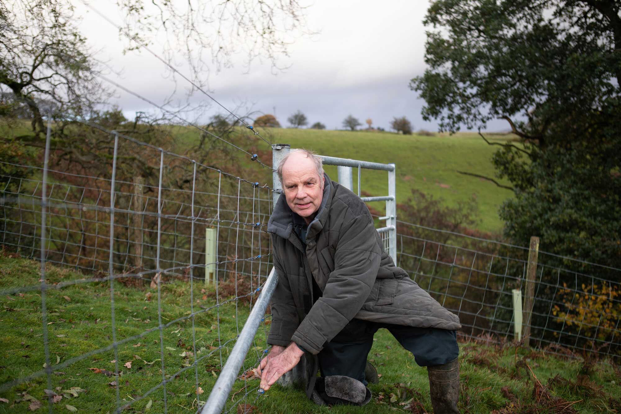 Portrait photo of Stephen Sanderson kneeling next to a newly constructed metal fence. Credit Charlie Fox.