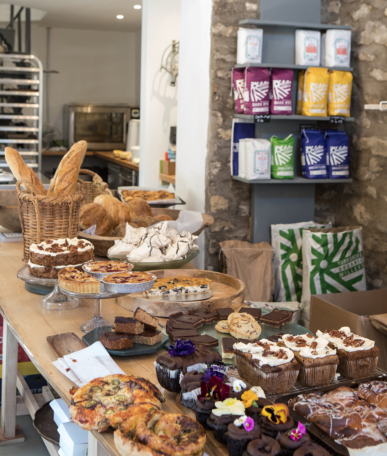 Baked goods on table and flour on shelving behind by Polly Baldwin