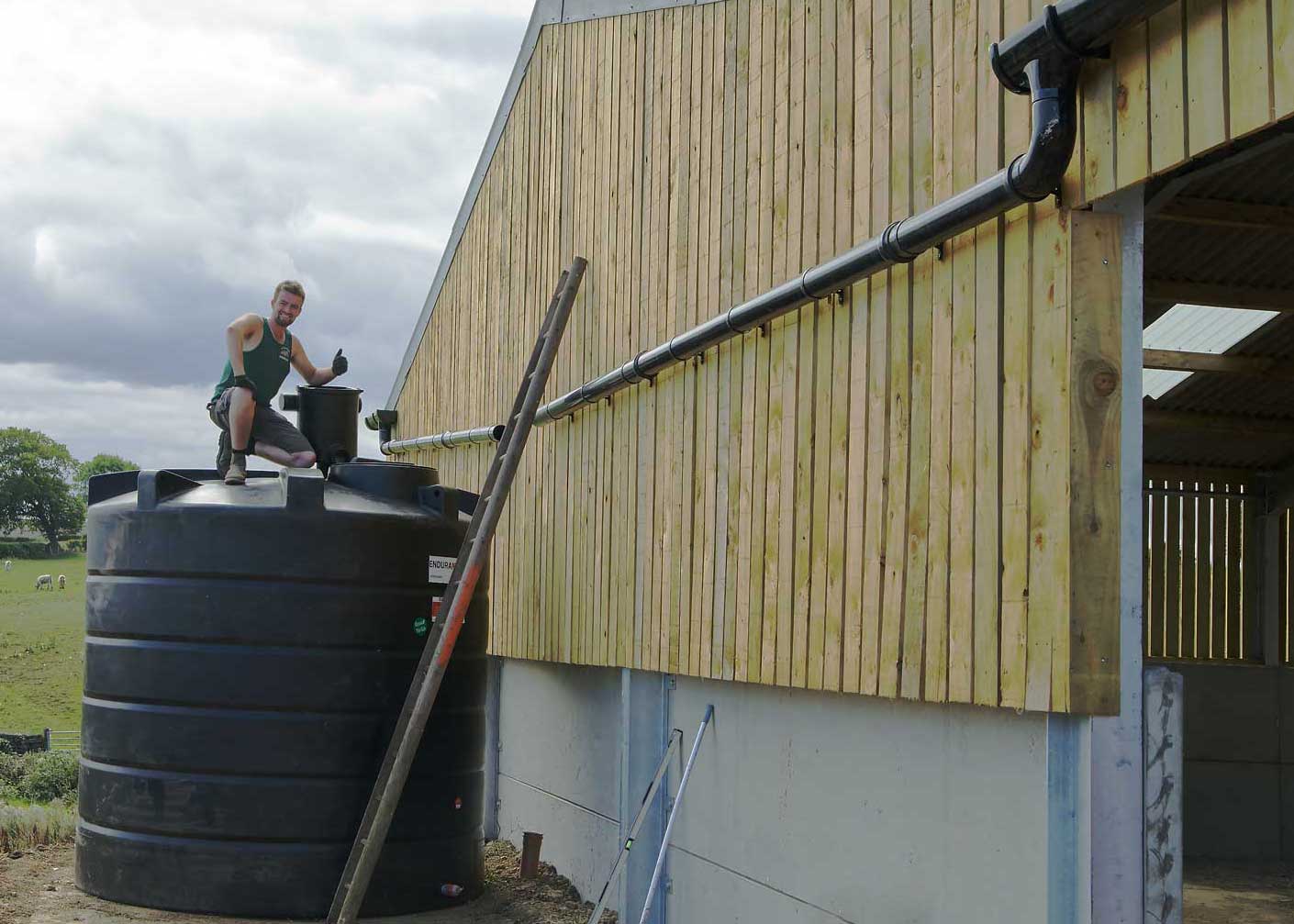 Man standing on top of a newly installed rainwater harvester next to a barn.